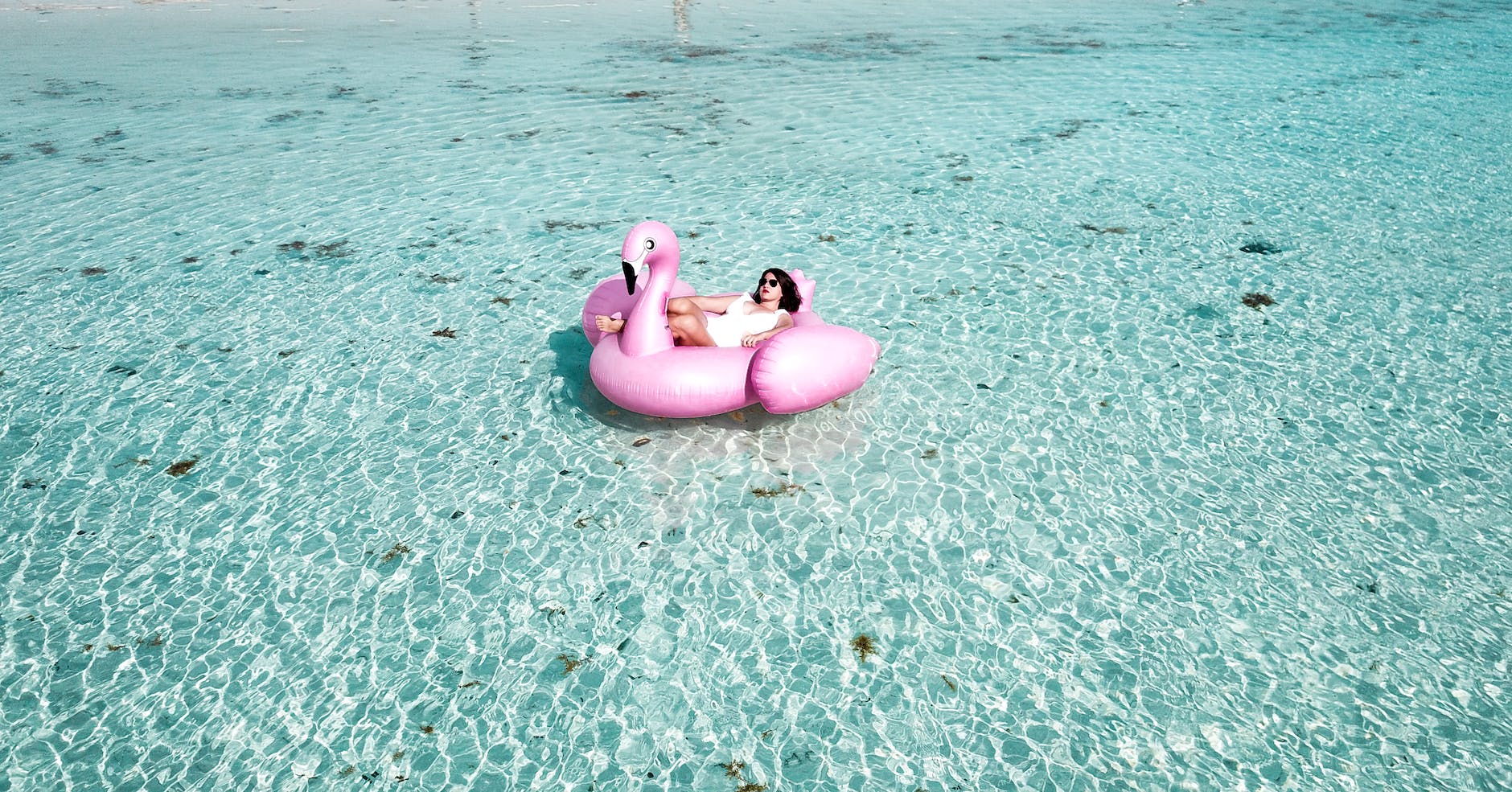 woman lying on pink flamingo bouy on body of water